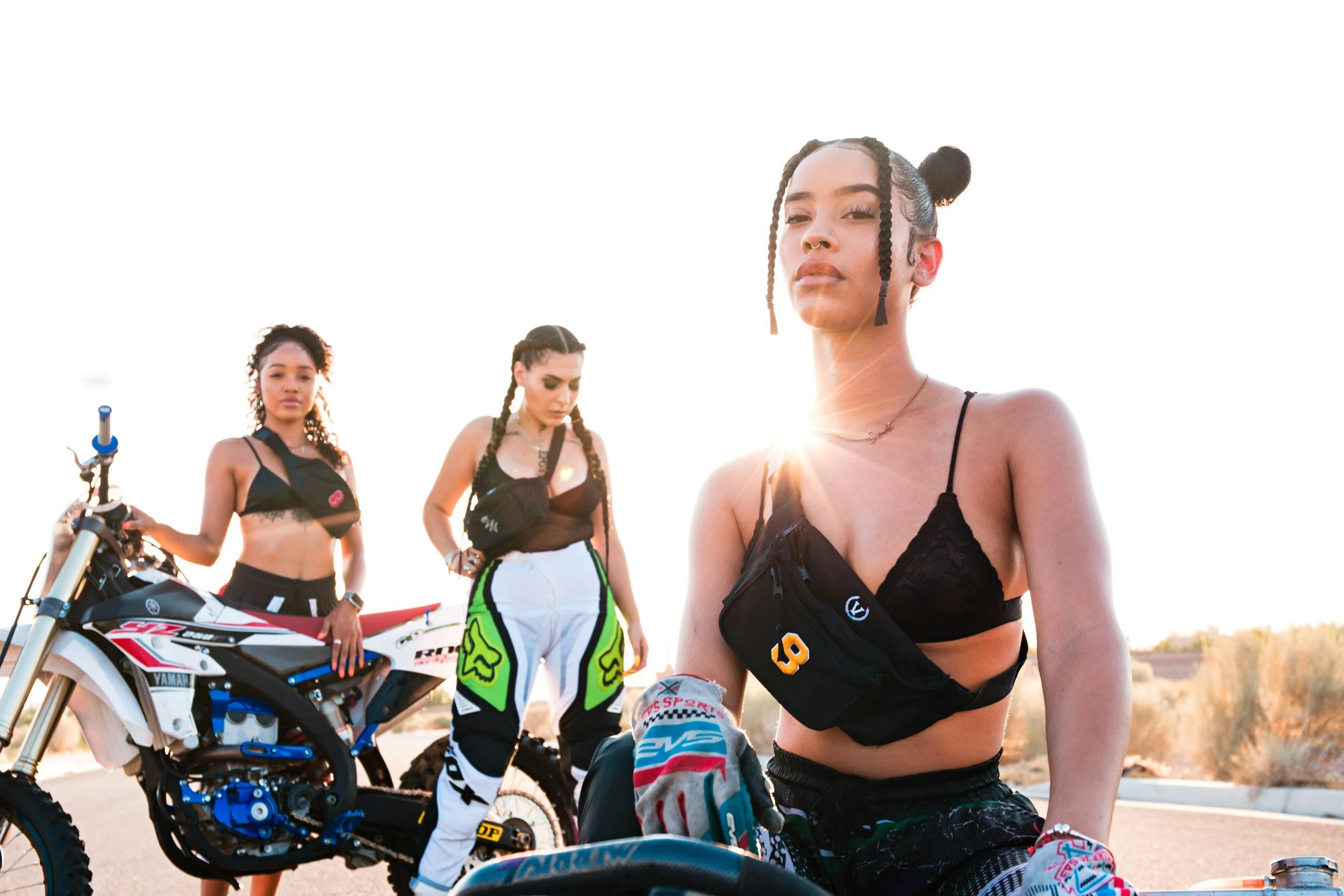 Women riders posing with street legal dirt bikes outdoors in desert setting during golden hour