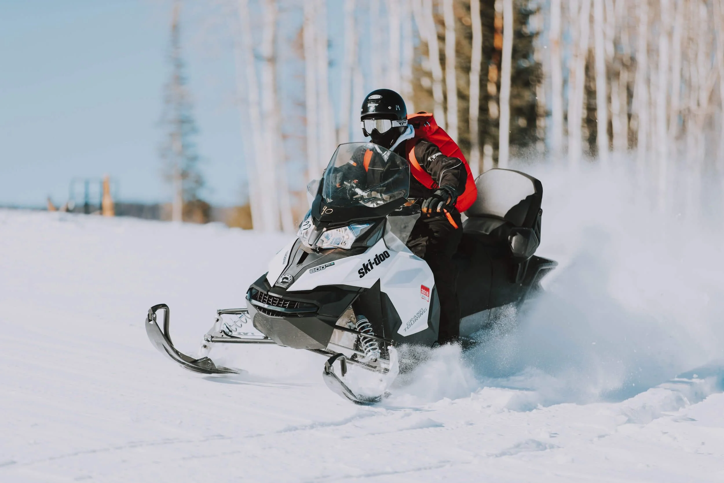 Person riding white and black Ski-Doo snowmobile through snowy forest terrain during winter sledding season