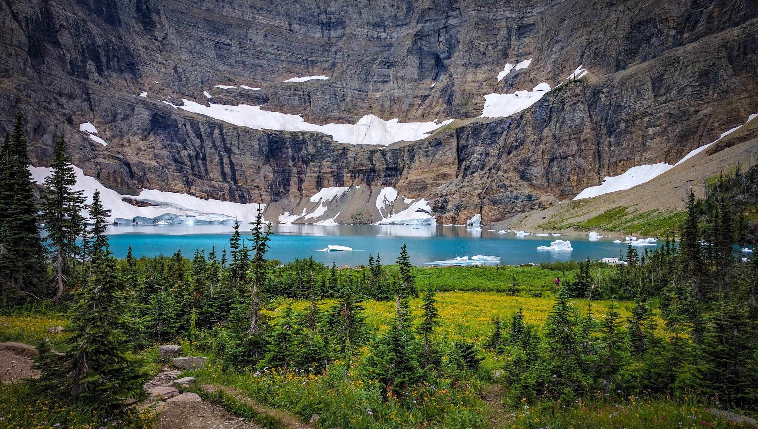 Alpine glacier lake surrounded by evergreen forest and snow-capped mountain peaks in Montana wilderness landscape