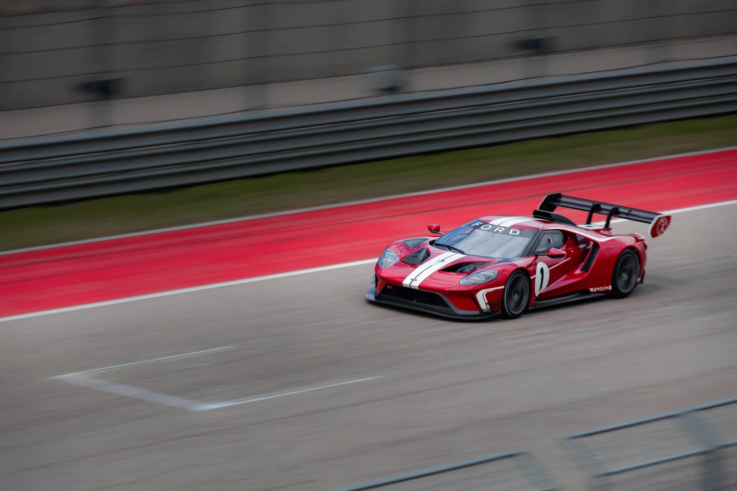 Red Ford GT race car with white stripe driving on track with red curbing, demonstrating street legal performance vehicle.