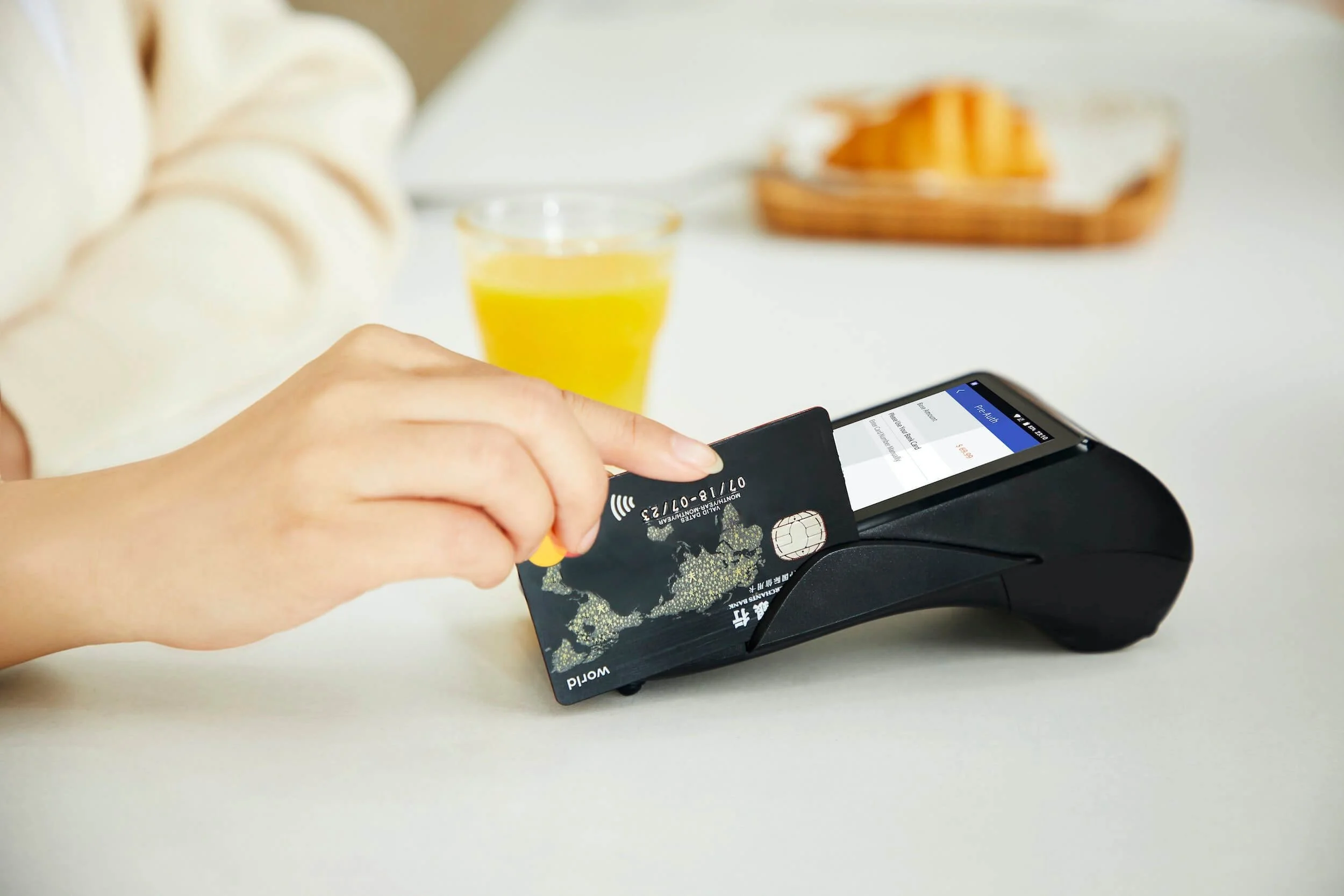 Woman tapping credit card on payment terminal during breakfast, demonstrating contactless transaction security.