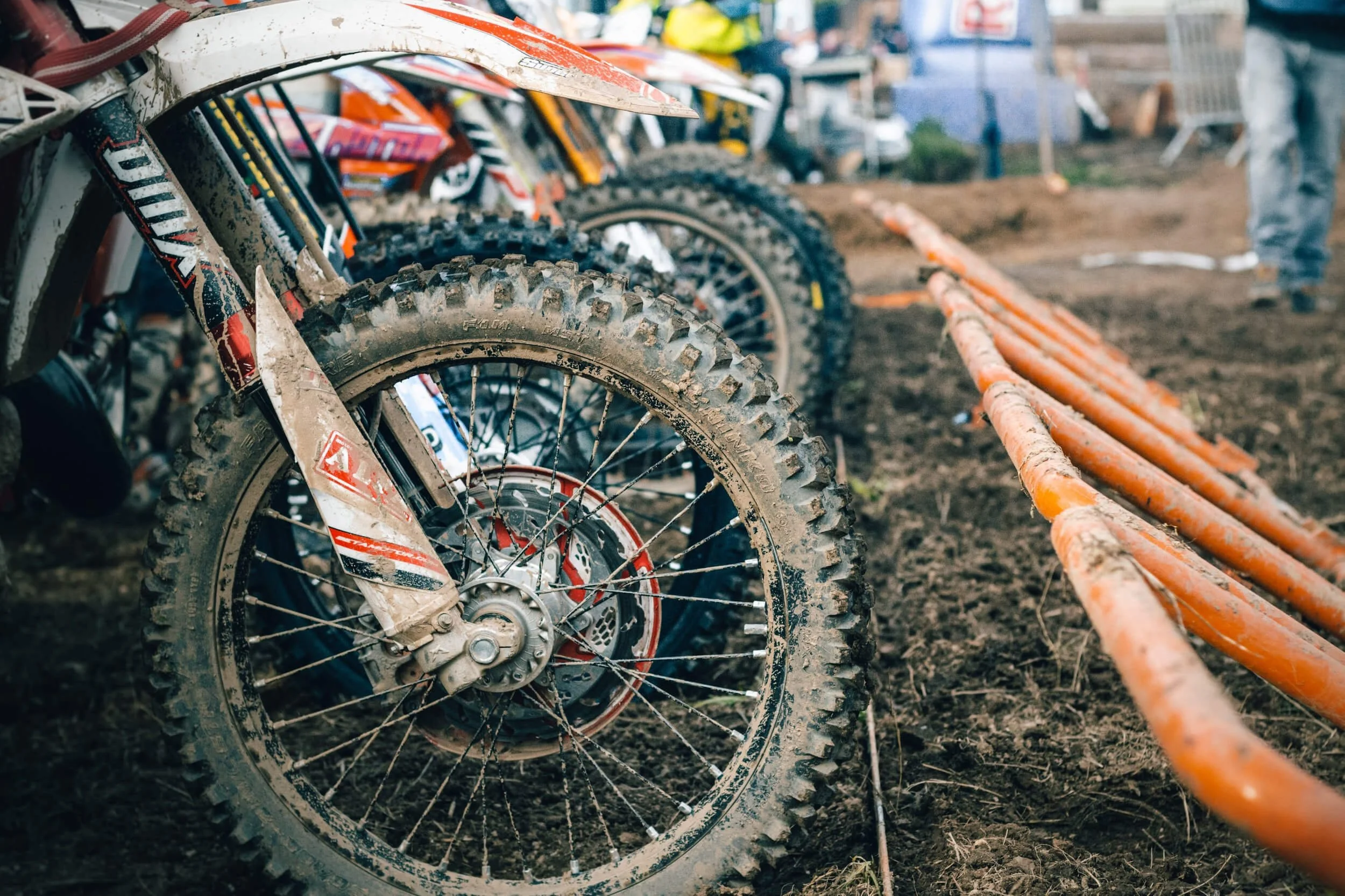 Muddy dirt bike wheel at motocross event track, showing off-road tires and suspension ready for registration.