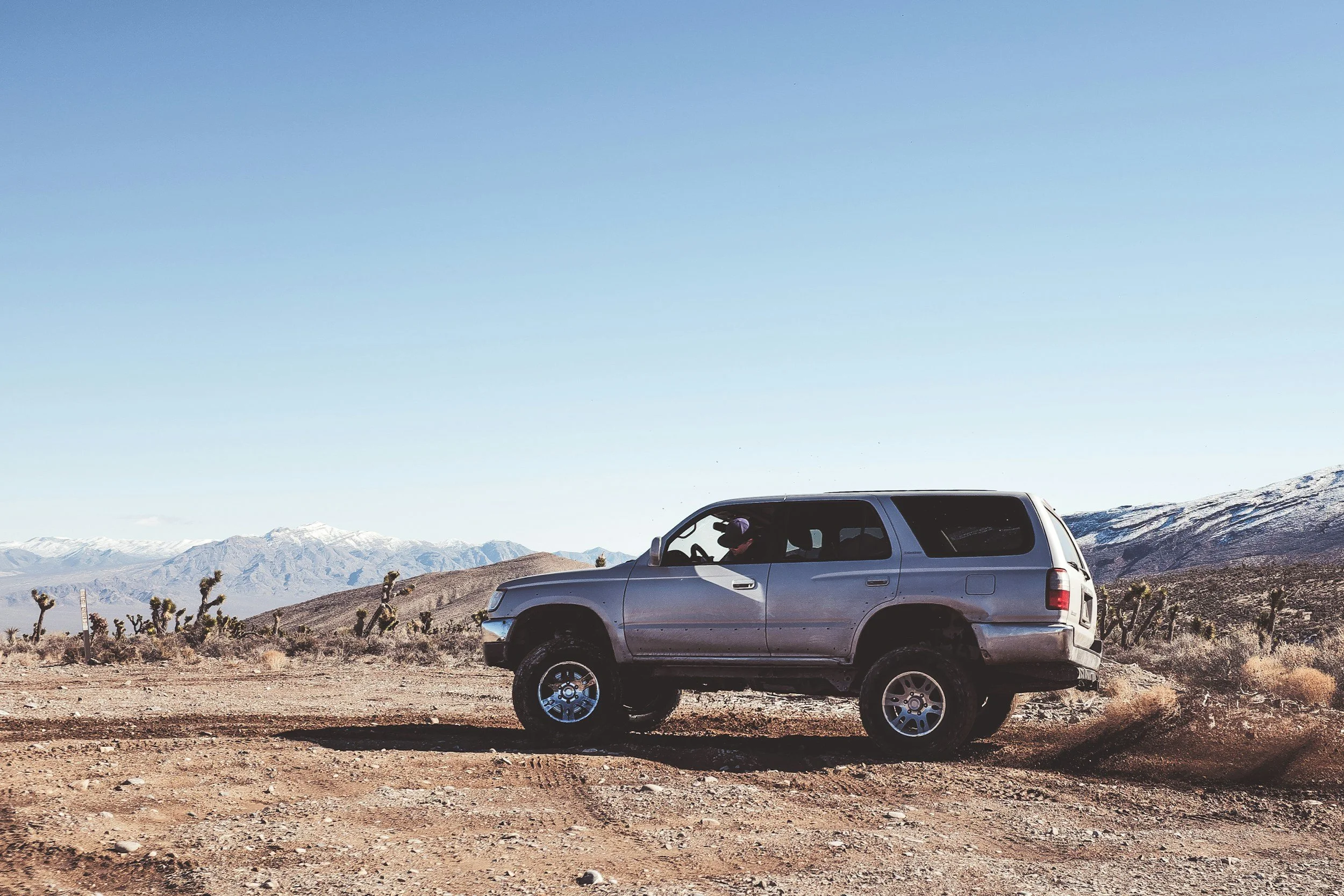 Blue SUV parked on desert road with snow-capped mountains, vehicle registration and South Dakota relocation concept