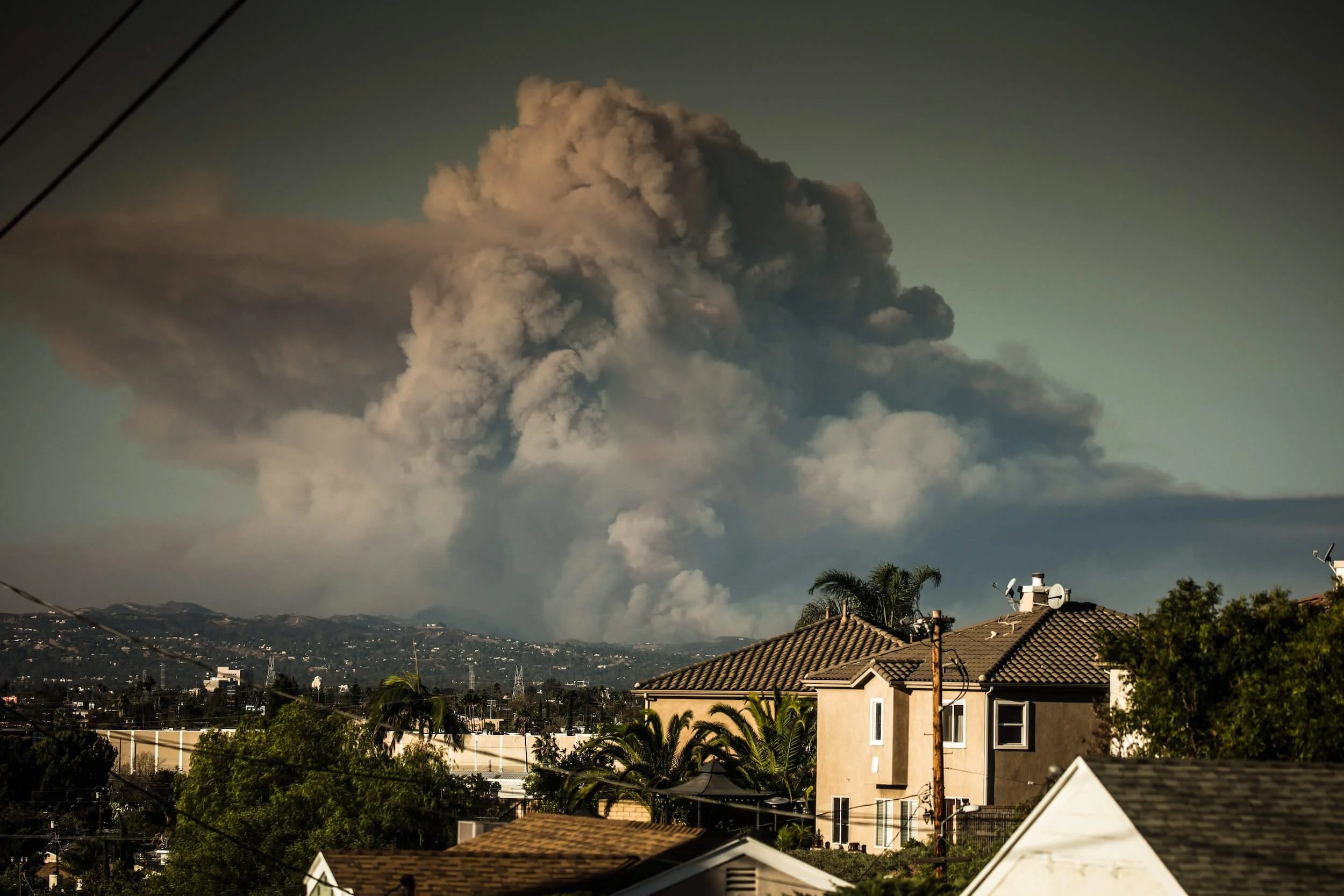Residential neighborhood with houses and palm trees during California wildfire smoke plume in distance