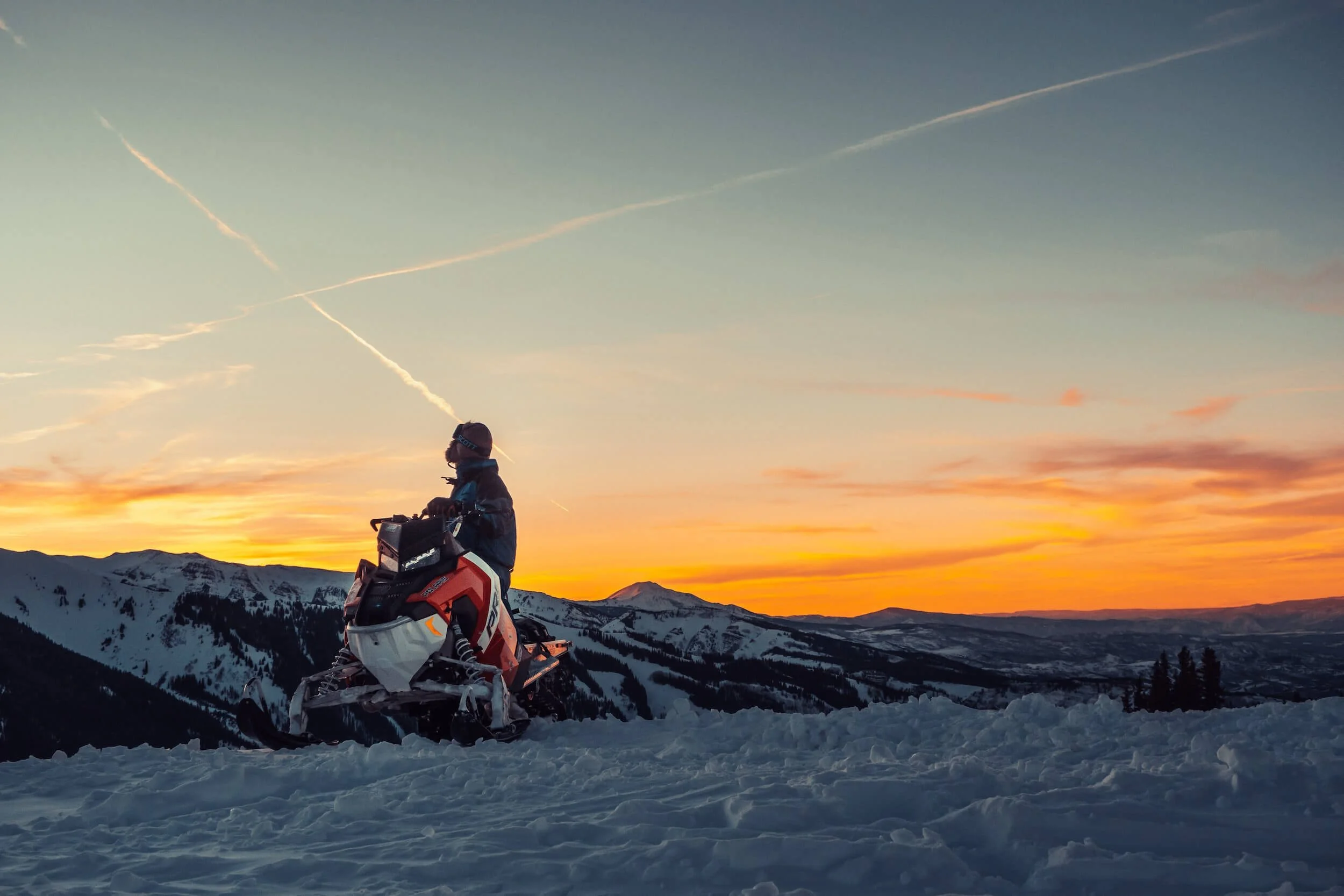 Snowmobiler riding red and white snowmobile on snowy mountain at sunset during winter adventure