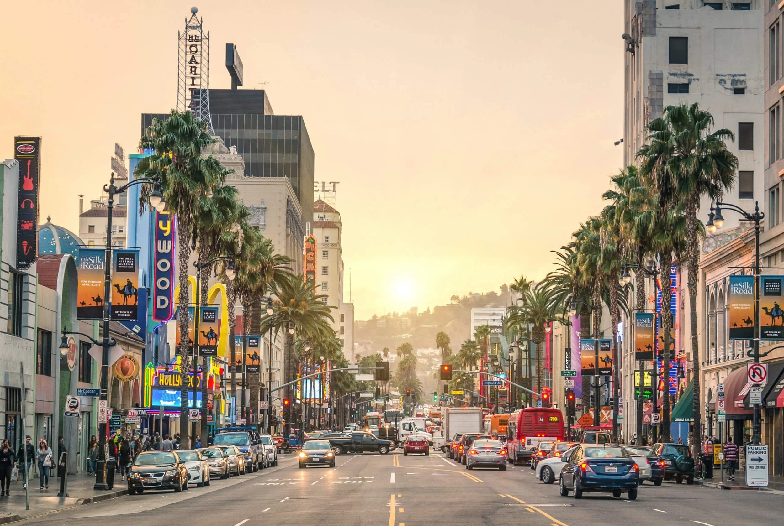 Hollywood Boulevard in Los Angeles with cars, palm trees, and colorful theater signs during sunset