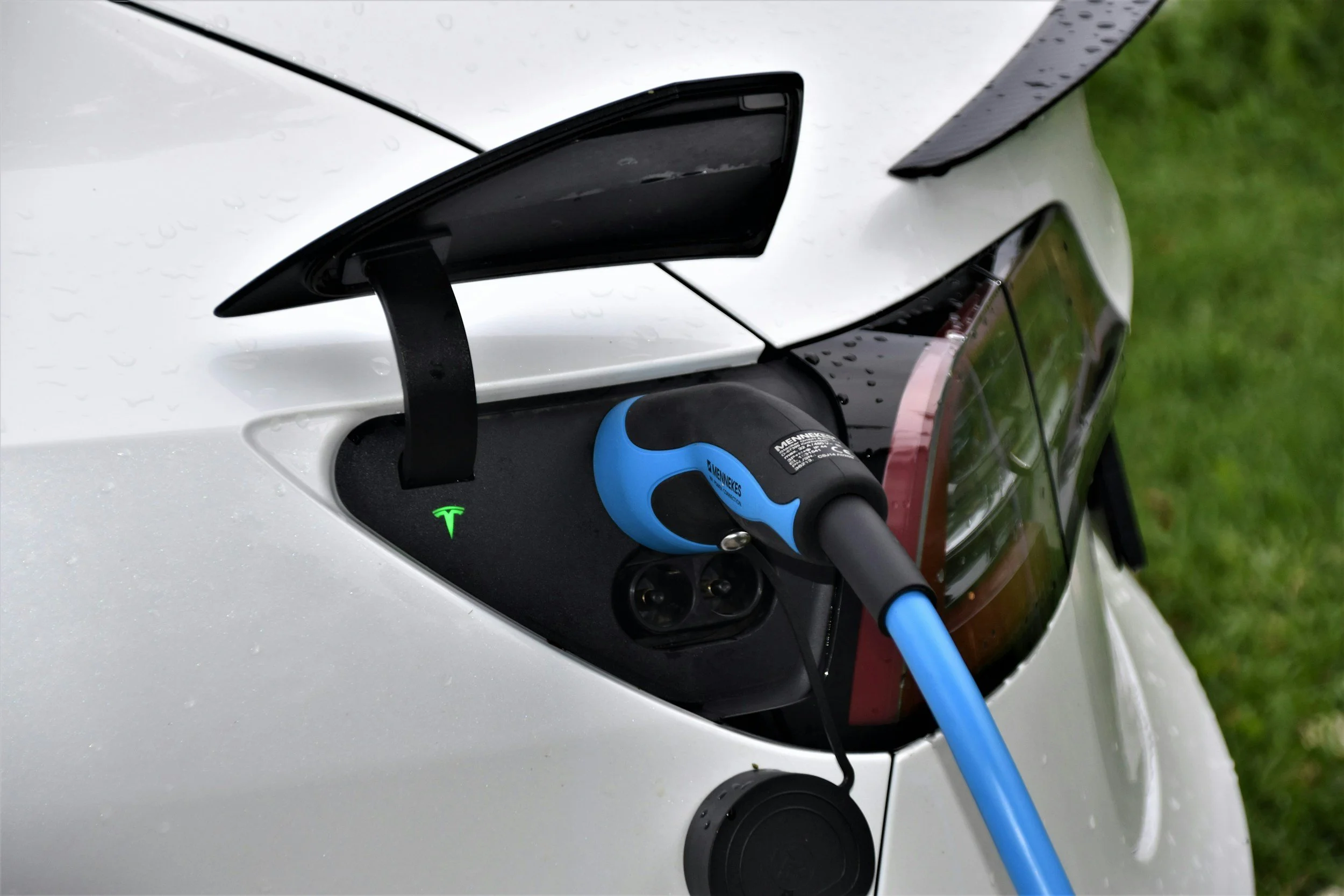 Tesla electric vehicle charging with blue connector cable plugged into port outdoors