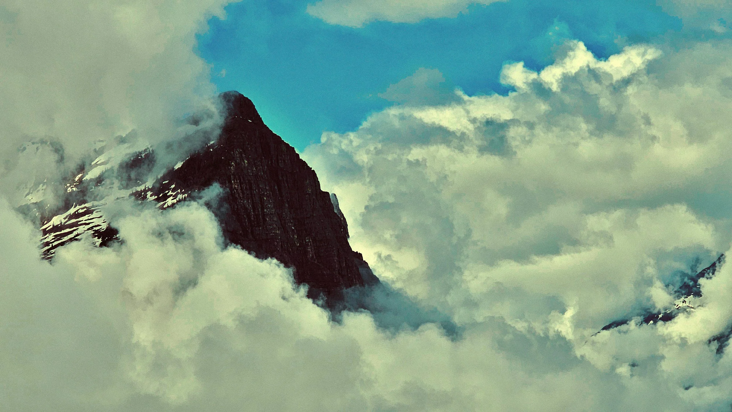 Snow-capped mountain peak emerging from clouds in Montana wilderness landscape for hunting guide series