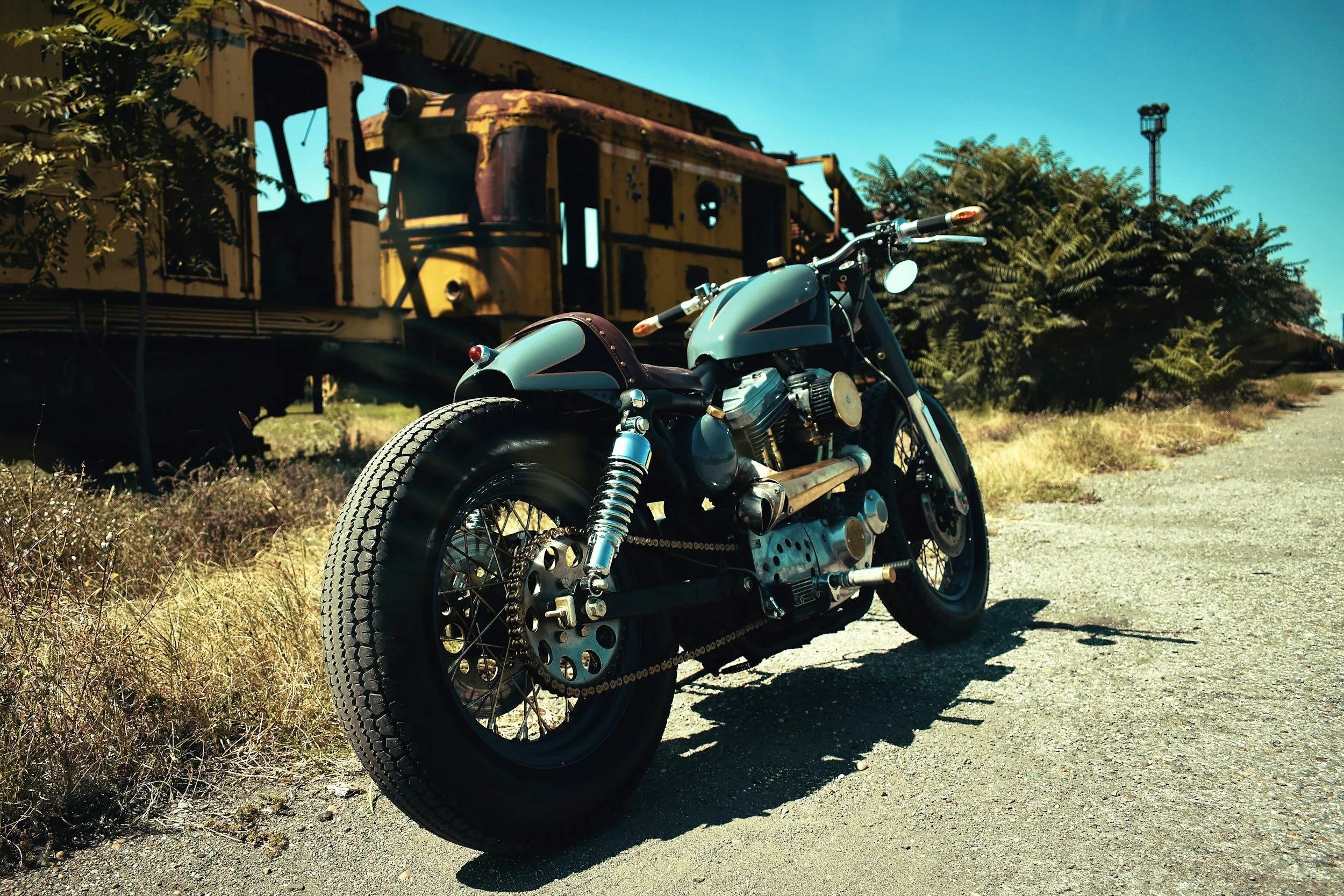 Custom bobber motorcycle parked on rural road near abandoned train car