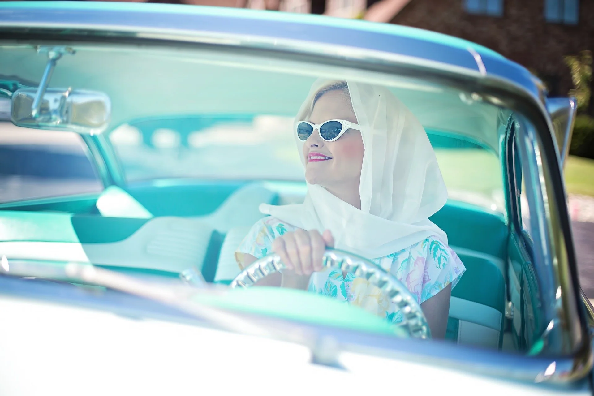 Stylish woman driving turquoise convertible car in sunny outdoor setting, transferring vehicle ownership concept