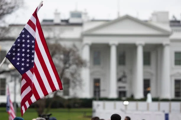 American flag waves in front of White House symbolizing presidential automotive industry policy and executive orders.