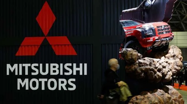 Red Mitsubishi off-road truck climbing large rock at auto show