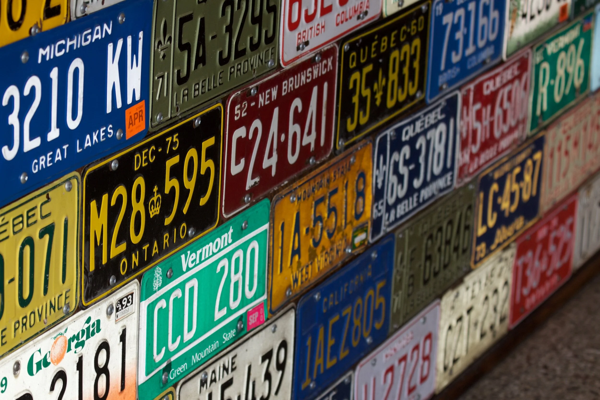Collection of colorful Canadian and US vehicle license plates displayed on wall showing different provinces and states