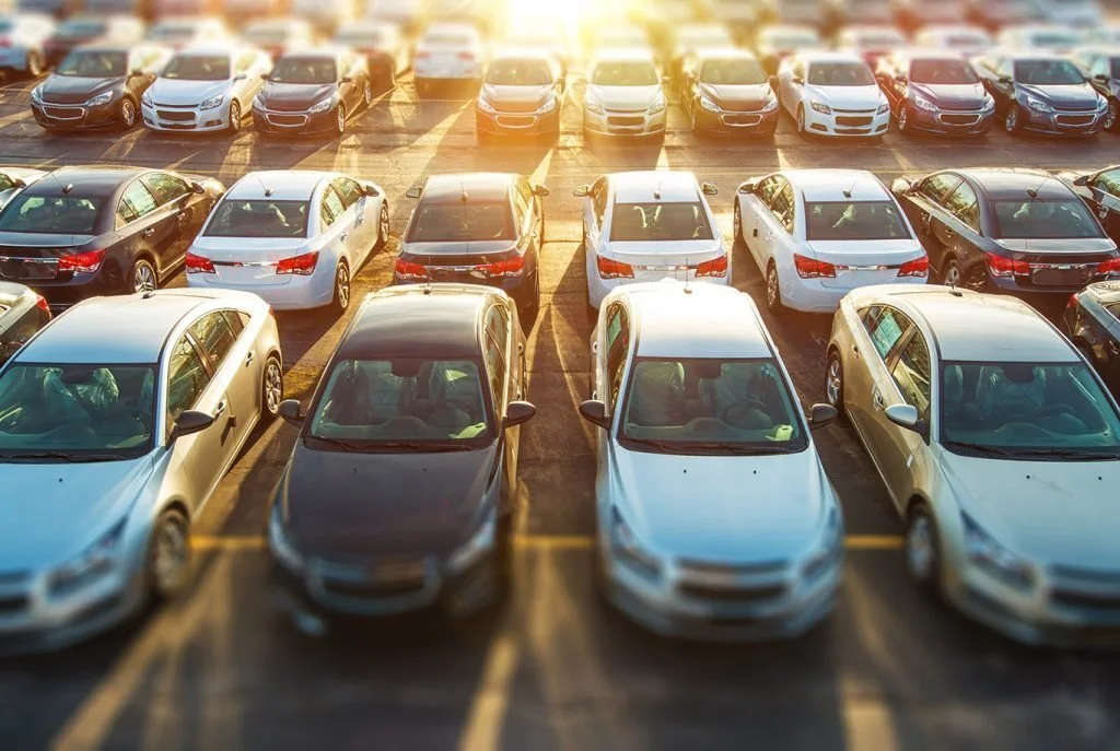 New cars lined up in dealer lot during sunset, reflecting Biden administration vehicle sales regulations ruling.
