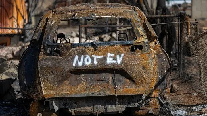 Burned-out vehicle marked "NOT EV" amid California wildfire debris from lithium-ion battery cleanup efforts
