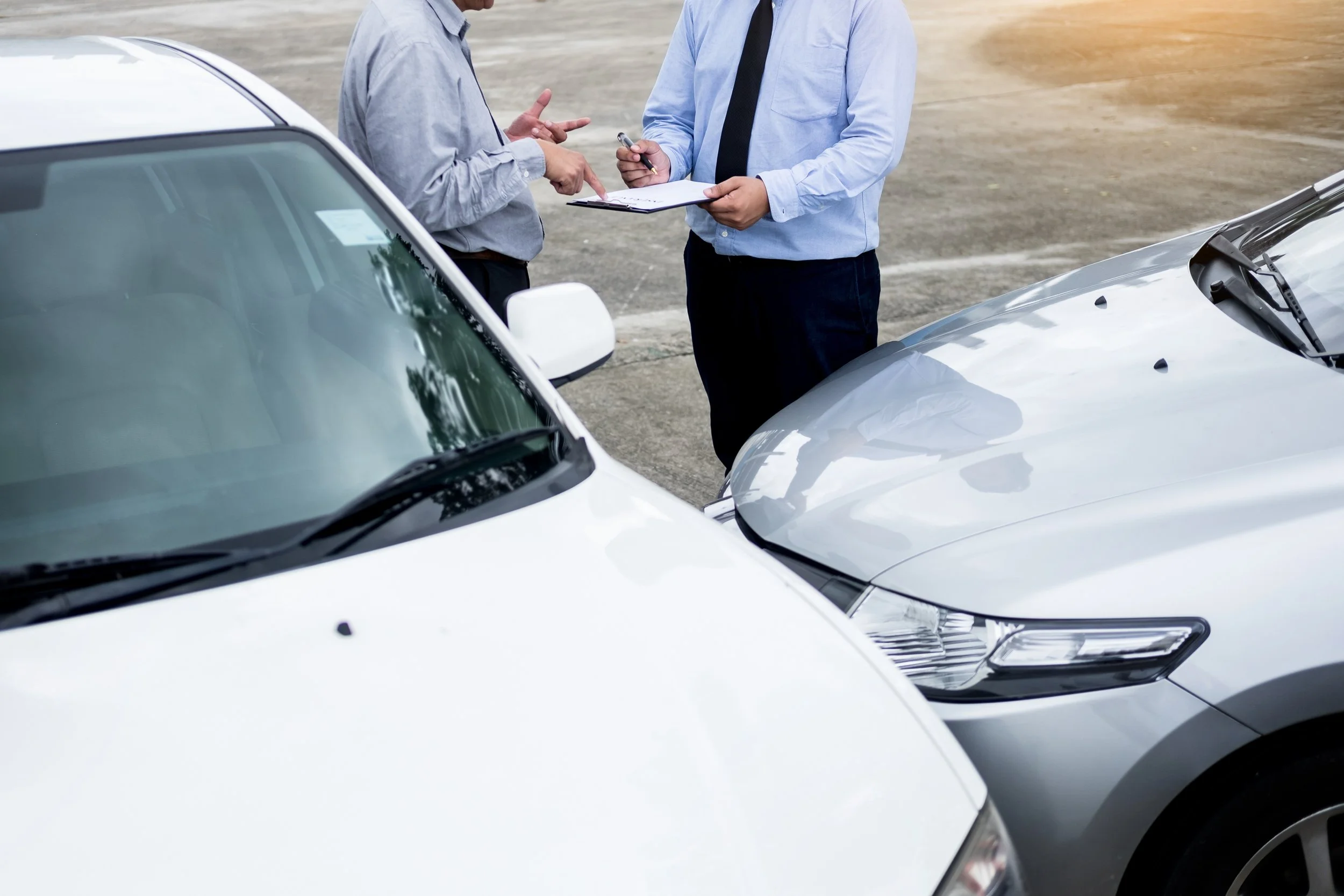 Two insurance adjusters documenting car accident damage between white vehicles in parking lot