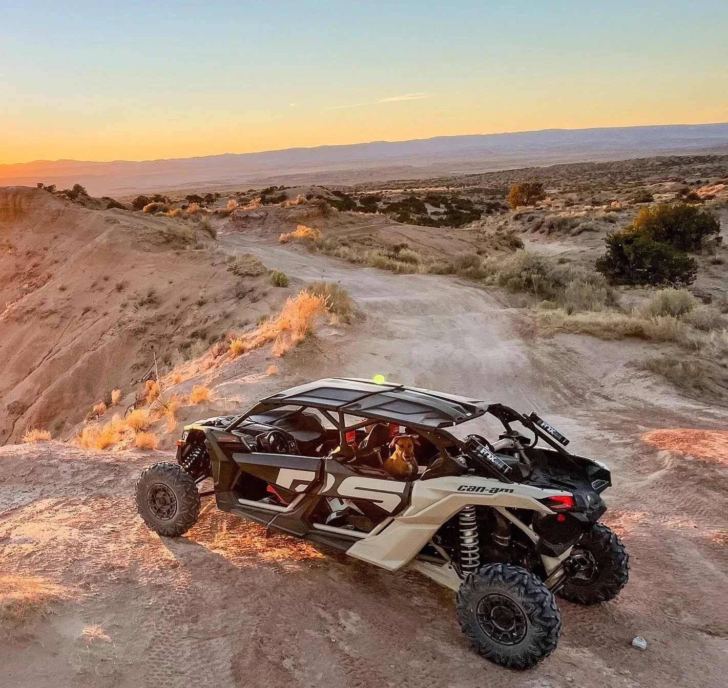 Can-Am side-by-side vehicle parked on desert terrain at sunset overlooking vast landscape and mountains