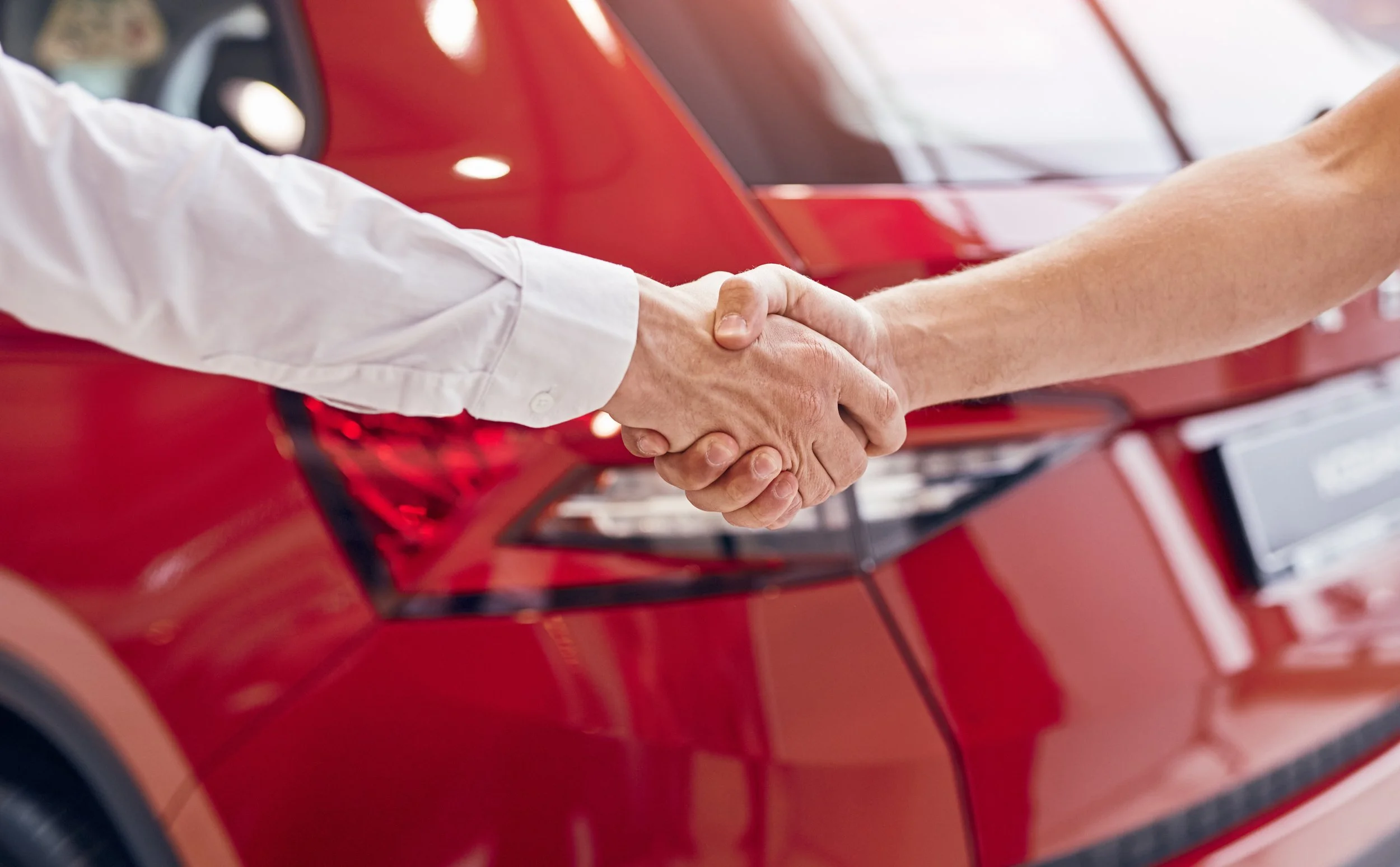 Handshake between car buyer and salesman in front of red vehicle at dealership