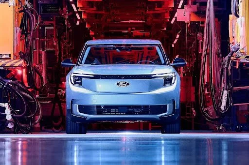 Ford electric vehicle on manufacturing assembly line with red industrial lighting and equipment