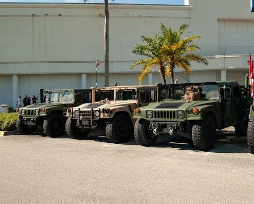 Three military Humvees parked in desert tan and olive green colors at outdoor facility with palm tree