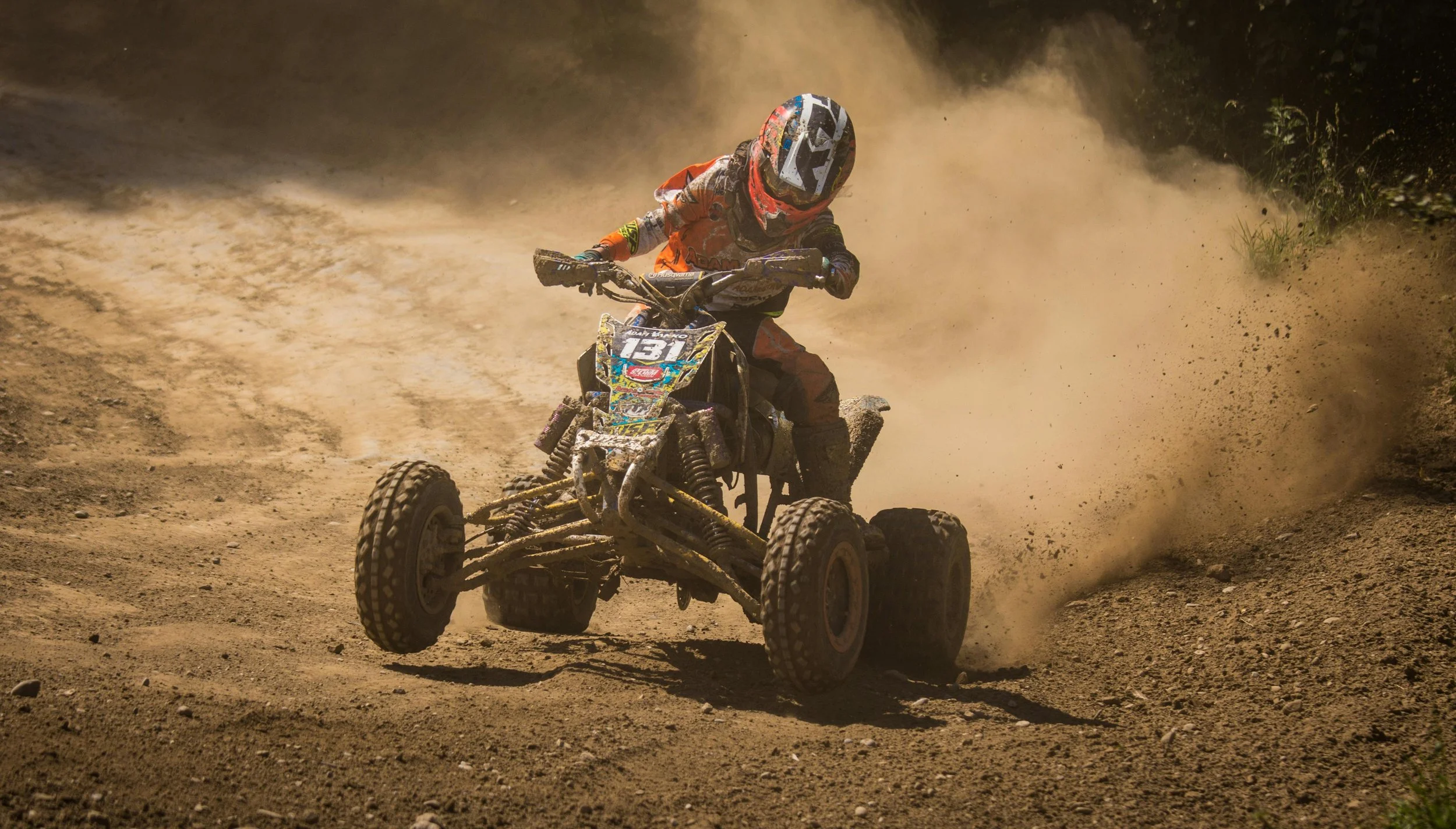 ATV rider in red gear racing through dusty dirt trail, demonstrating off-road vehicle performance and capability.