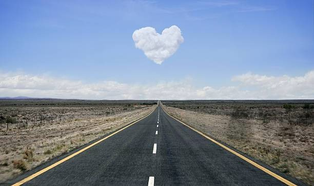 Straight desert highway with heart-shaped cloud symbolizing love and connection between driver and vehicle on open road.