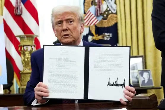 President Trump displays signed executive order on auto tariffs at Oval Office desk with American flags