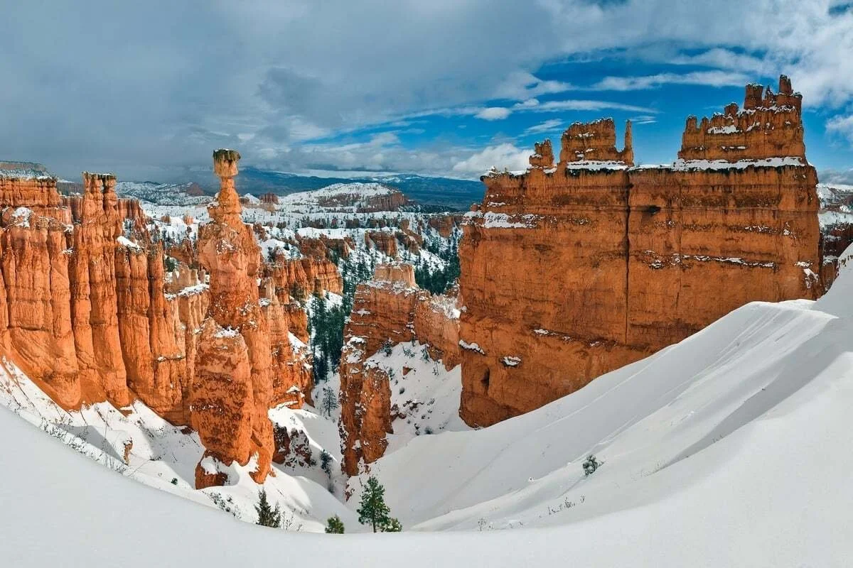 Snow-covered hoodoos at Bryce Canyon in winter, showcasing dramatic red rock formations dusted with white snow under blue sky