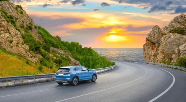 Blue SUV driving on coastal mountain road at sunset, representing smart vehicle investment and road trip planning