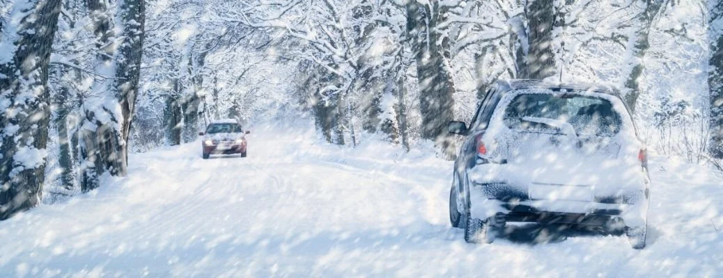 Cars driving on snowy forest road in winter weather conditions with snow-covered trees