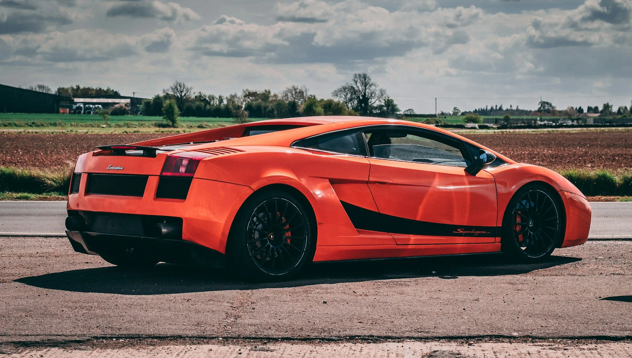 Red Lamborghini sports car parked on rural road with farmland background