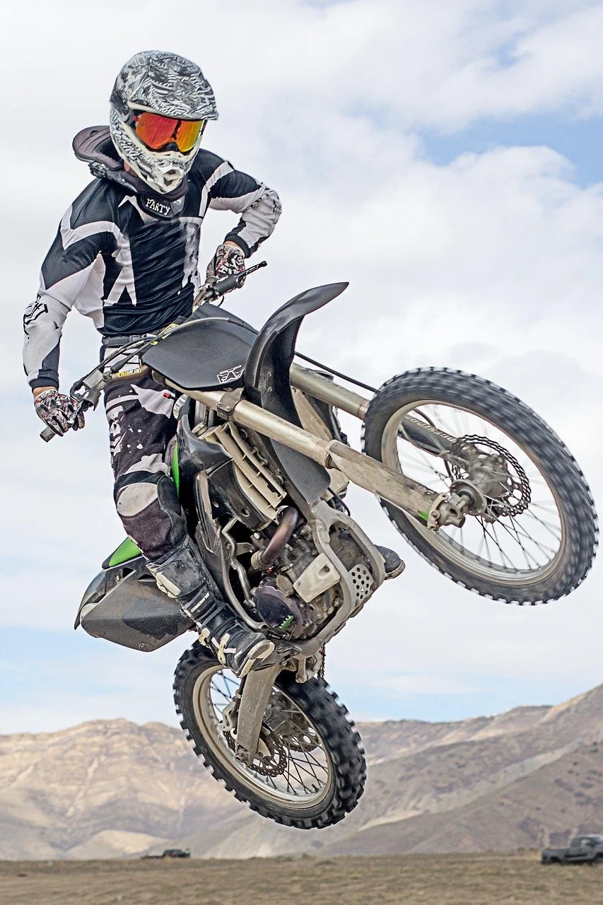 Dirt bike rider performing wheelie stunt in desert landscape with protective gear