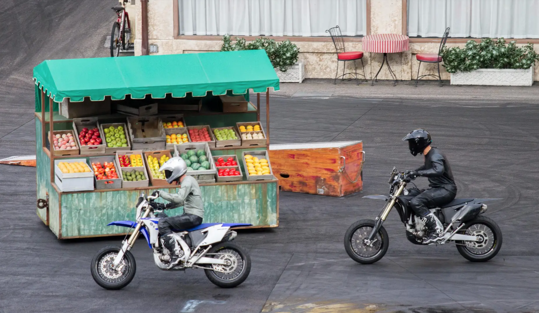 Stunt dirt bikes parked near a colorful fruit market stand in an urban plaza setting