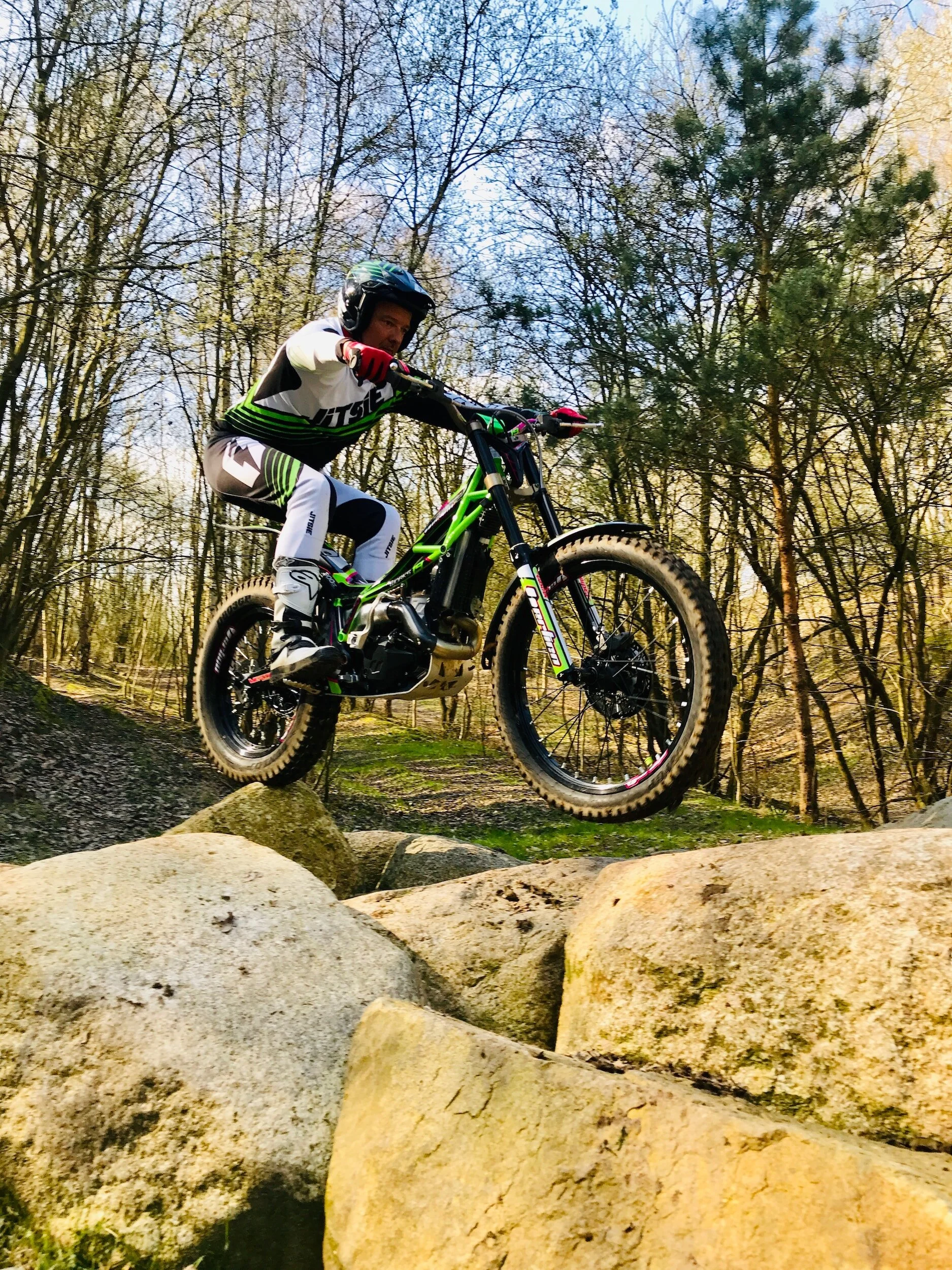 Mountain biker jumping over rocks on forest trail with green trials bike in action