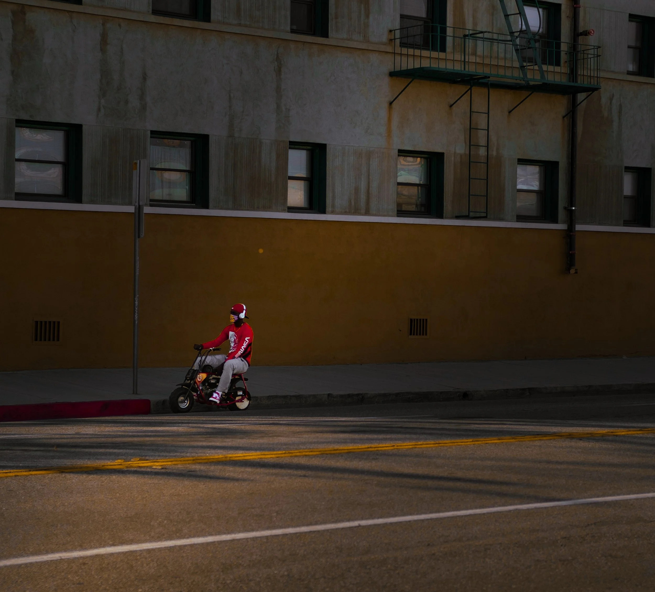 Red pit bike rider on urban street with yellow building, demonstrating street-legal pit bike riding in California