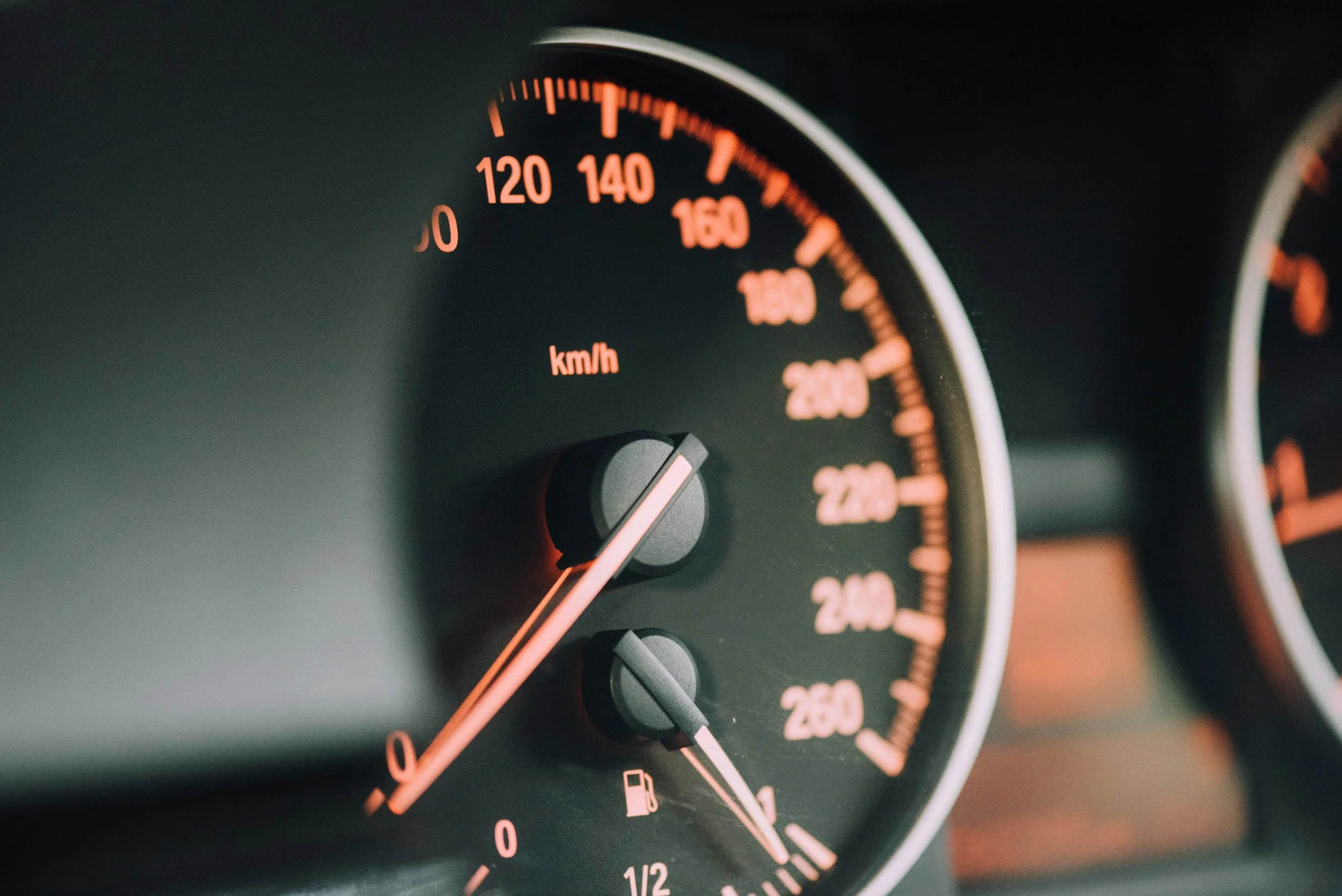 Close-up of car speedometer dashboard with orange gauges showing speed in km/h and fuel level indicator