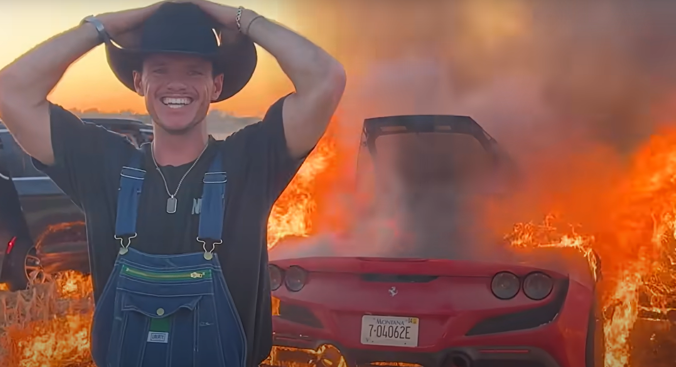 Man in cowboy hat poses with burning red Ferrari in desert flames and explosion scene