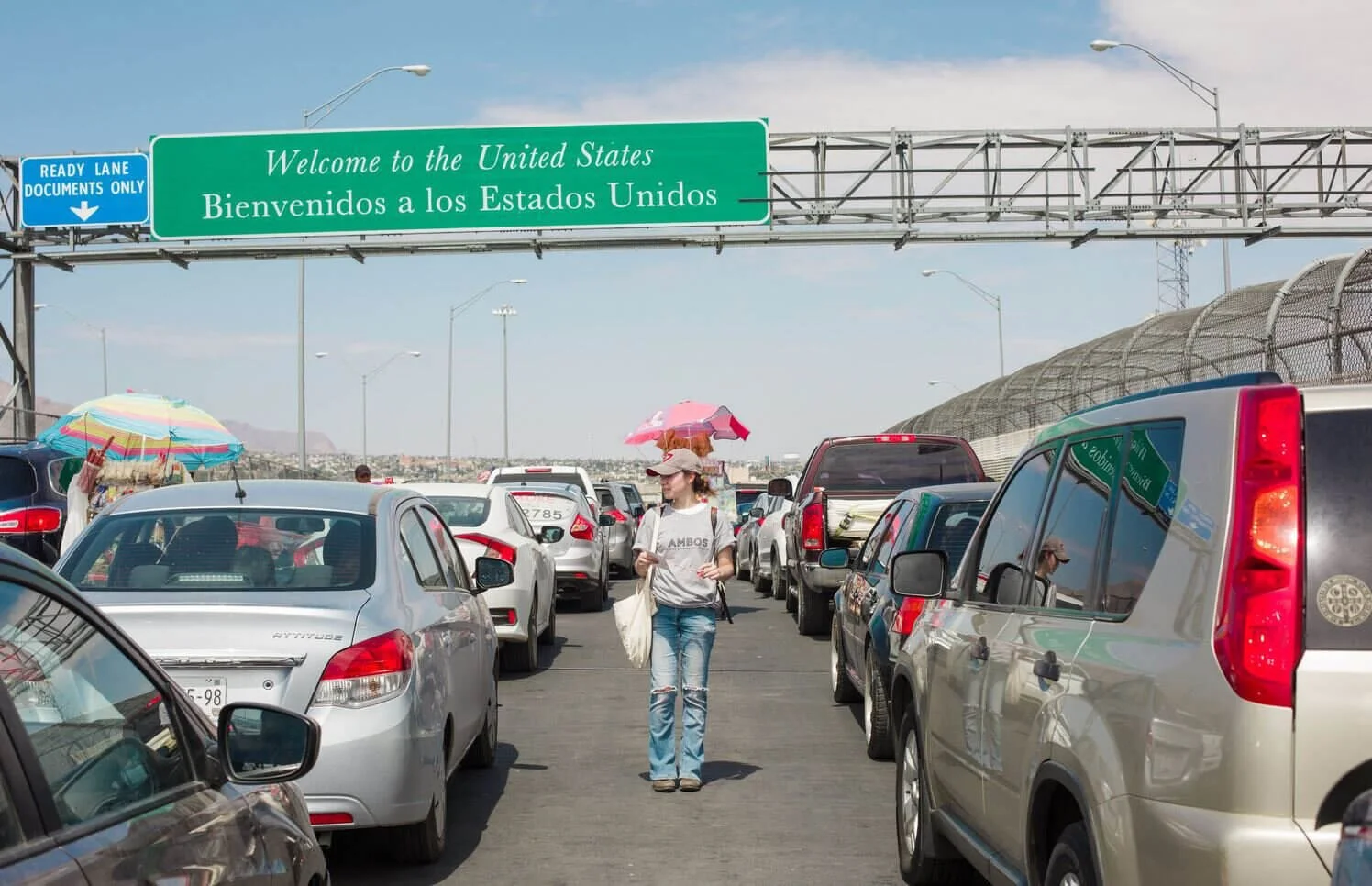Traffic jam at US-Mexico border crossing with welcome sign, cars lined up for vehicle import inspection