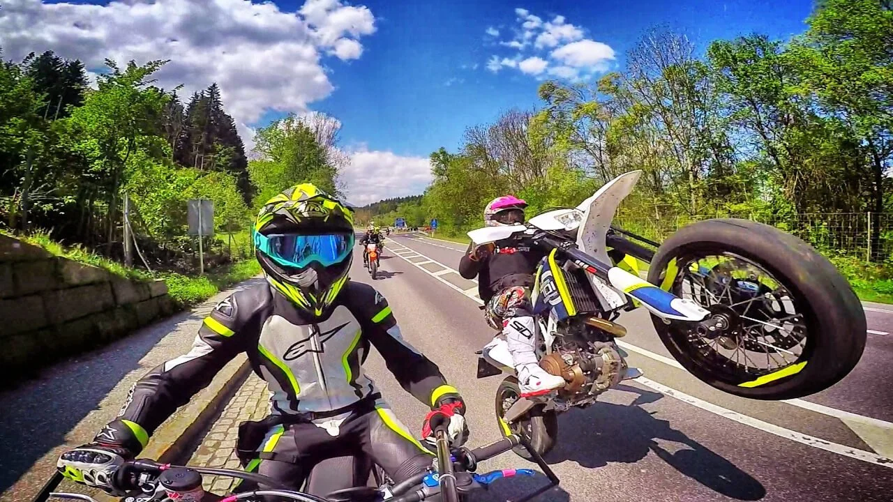 3 dirt bike riders on street, 1 doing wheelie