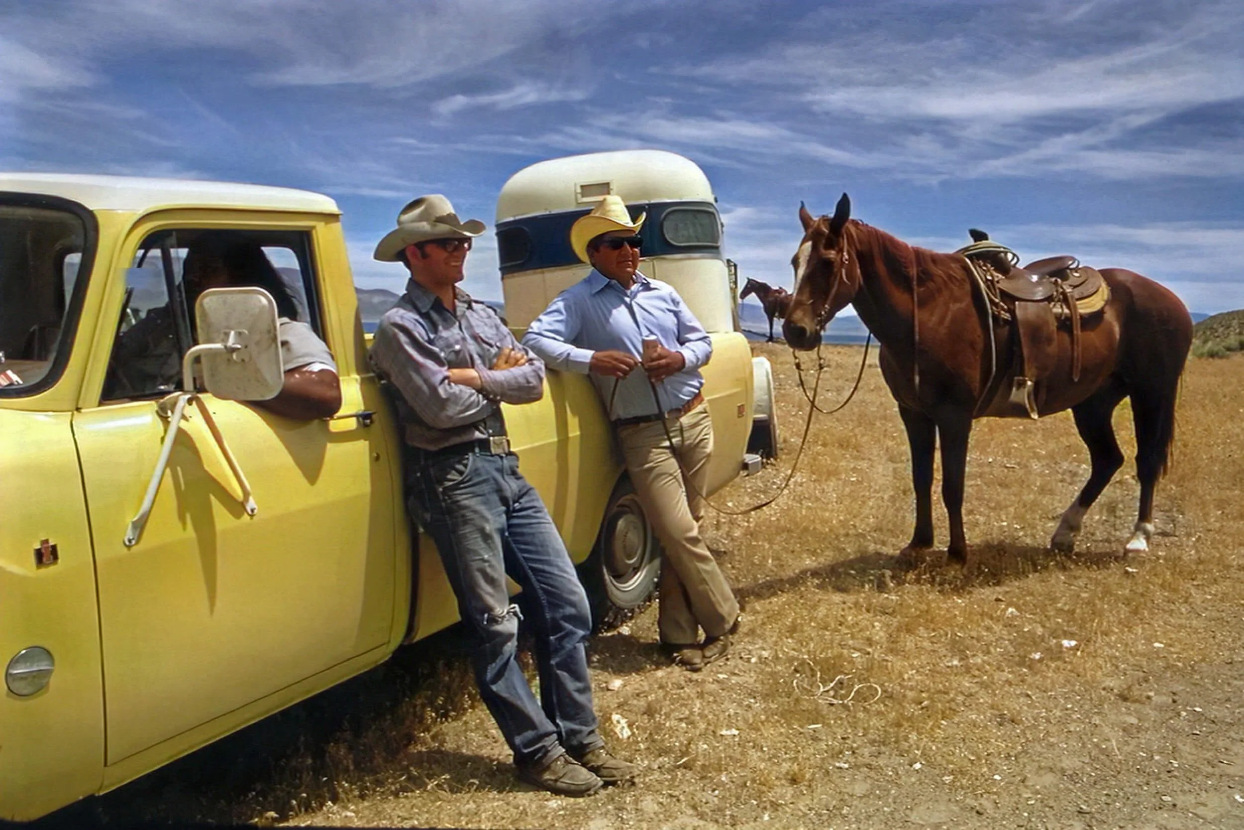 men standing beside yellow truck with horse