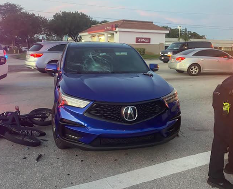 Blue Acura sedan involved in motorcycle safety accident with bike debris visible