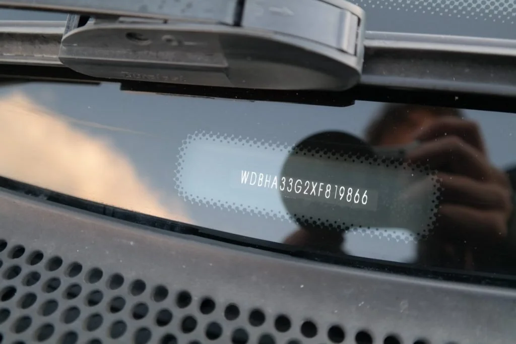A VIN plate photographed through the windshield on the lower driver's side of the dashboard