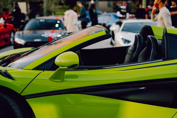 Lime green convertible sports car at exotic car collection event with elevated vehicles displayed in background